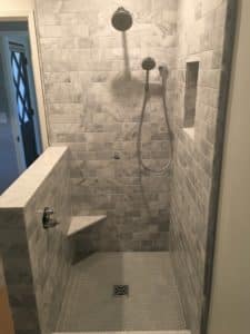 An open shower with light grey tile and an open wall. 