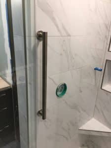 The image shows a white marbled shower with a long handle for accessibility. 