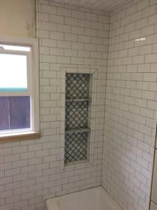 Image shows a shower with white, squared tiles. The shower also features a rectangular hole for storage. 