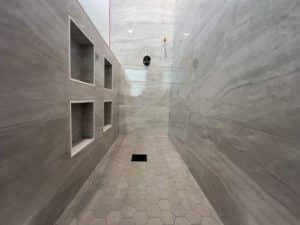 A modern, spacious shower with large grey tiles, featuring built-in wall shelves, and a hexagonal tiled floor.
